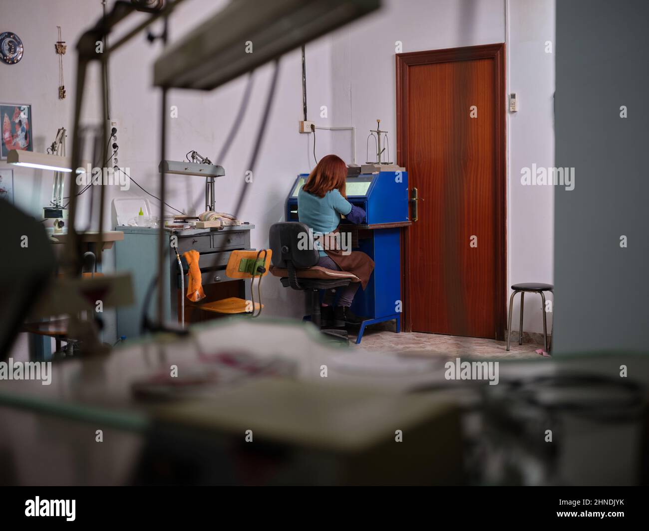 Eine nicht erkennbare Erwachsene Frau, die in ihrer Schmuckwerkstatt in einer Poliermaschine mit Sicherheitsbox sitzt Stockfoto