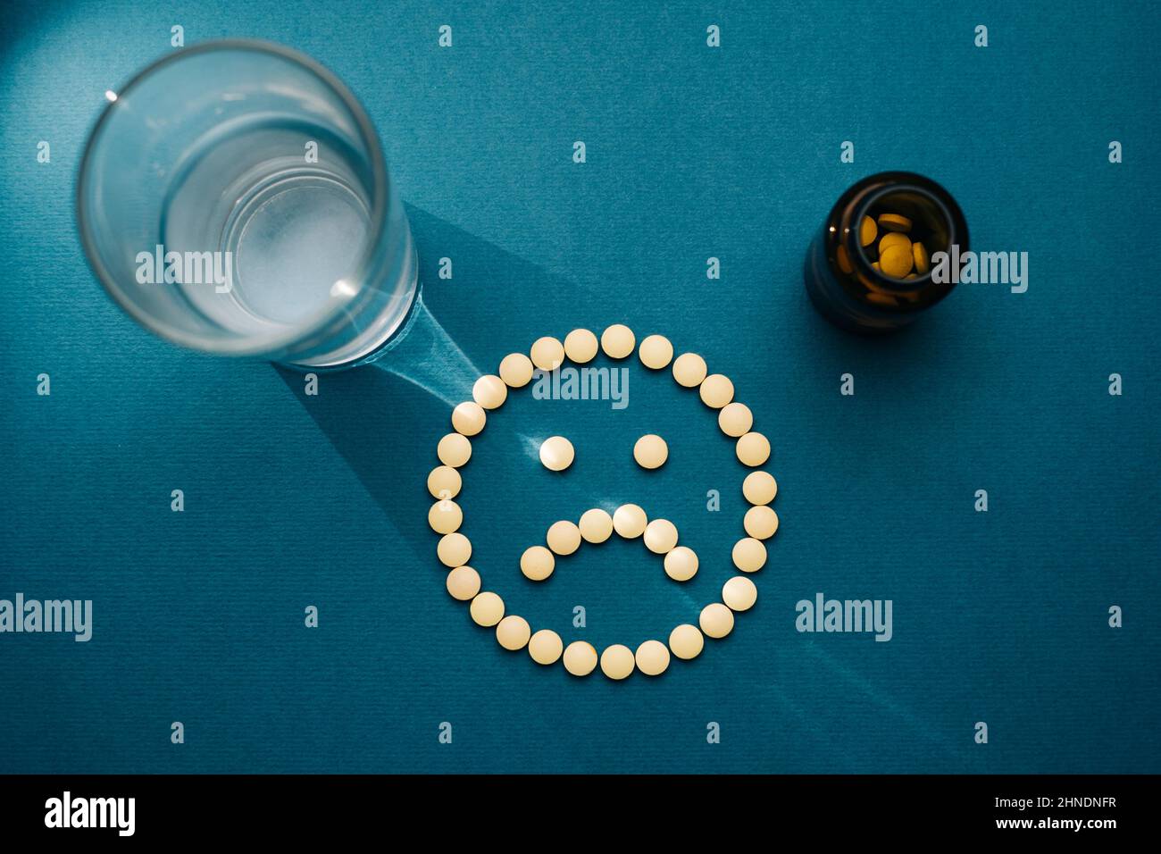Die Pillen sind auf einem blauen Hintergrund in Form eines traurigen Emoticons ausgelegt. Stockfoto
