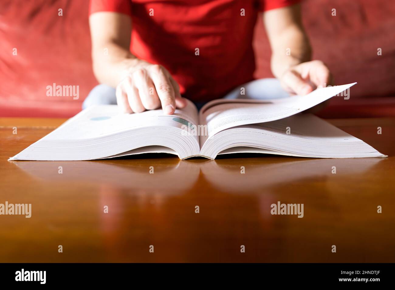 Eine Person in einem roten Hemd konsultiert die Lösung in einem Buch und findet sie, verschwommener Hintergrund, selektiver Fokus Stockfoto