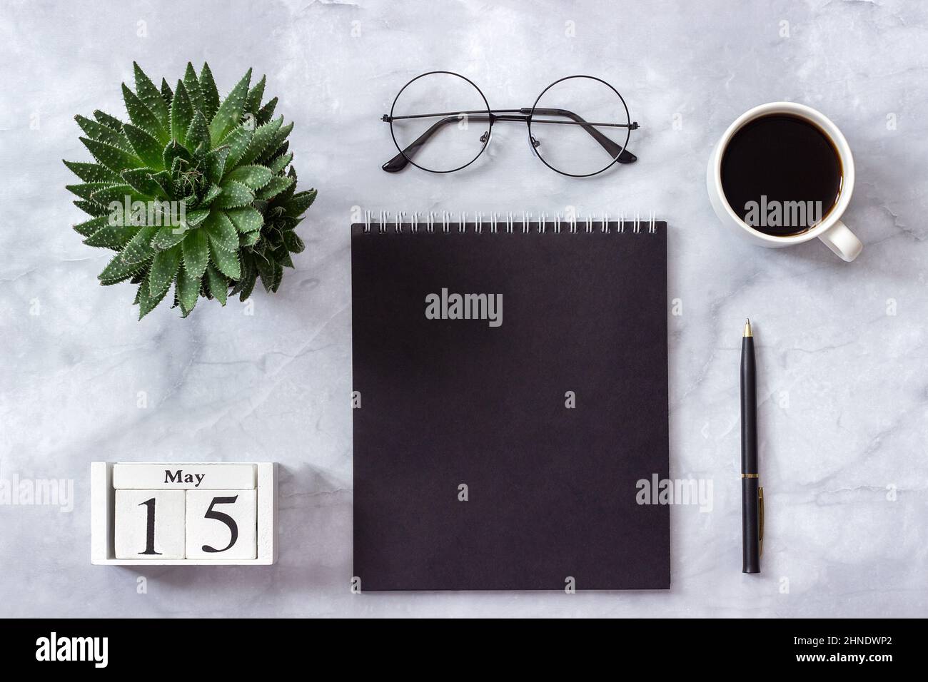 Schreibtisch im Büro oder zu Hause. Holzwürfel Kalender Mai 15. Schwarzer Notizblock, eine Tasse Kaffee, Sukkkulent, Gläser auf Marmorhintergrund Konzept stilvolle Workpla Stockfoto