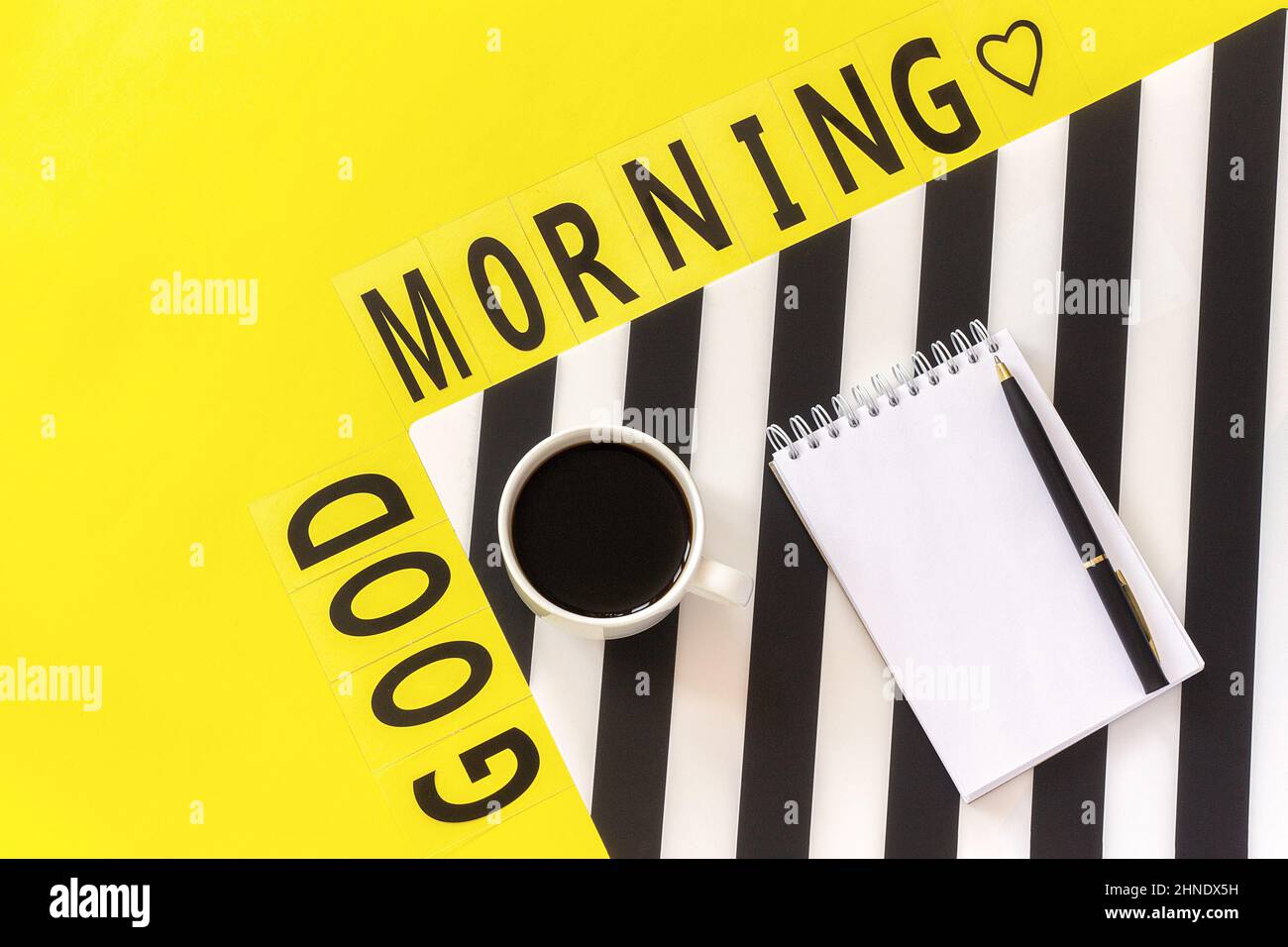 Text Guten Morgen, Kaffee, Notizbuch für Text auf stilvoller schwarz-weißer Serviette auf gelbem Hintergrund. Concept Guten Morgen. Stockfoto