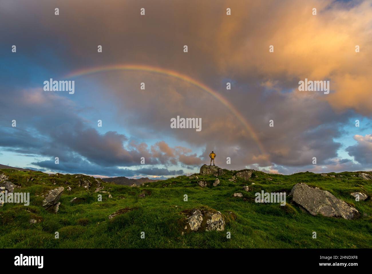 Ein Bergwanderer blickt auf einen Regenbogen auf schroffem Gelände in der Nähe von Ardara, County Donegal, Irland. Stockfoto