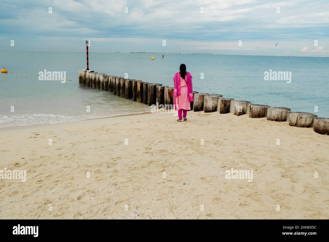 Frau in rosafarbenem Salwar Kameez, asiatische Tracht, die am Ufer von Kite Beach, Dubai, VAE, steht Stockfoto