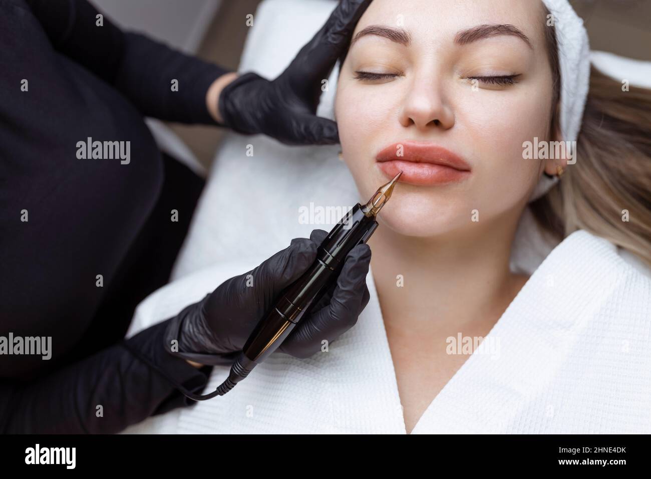 Der Kosmetologe macht dauerhaft Make-up auf dem Gesicht einer Frau. Spezialist trägt ein Tattoo auf die Lippen des Patienten Nahaufnahme Stockfoto