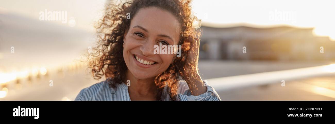 Porträt einer glücklichen Touristenfrau, einer fröhlichen Frau, die lächelt, während sie im Freien steht, um bei Sonnenuntergang in das Flugzeug zu steigen Stockfoto