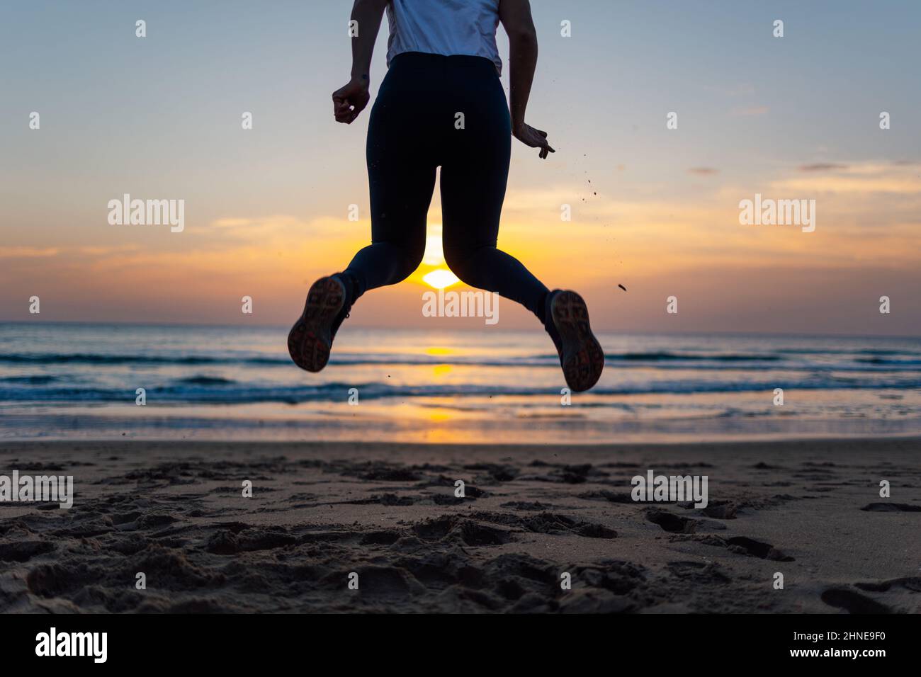 Nahaufnahme der Beine einer nicht erkennbaren jungen Frau, die bei Sonnenuntergang am Strand springt Stockfoto