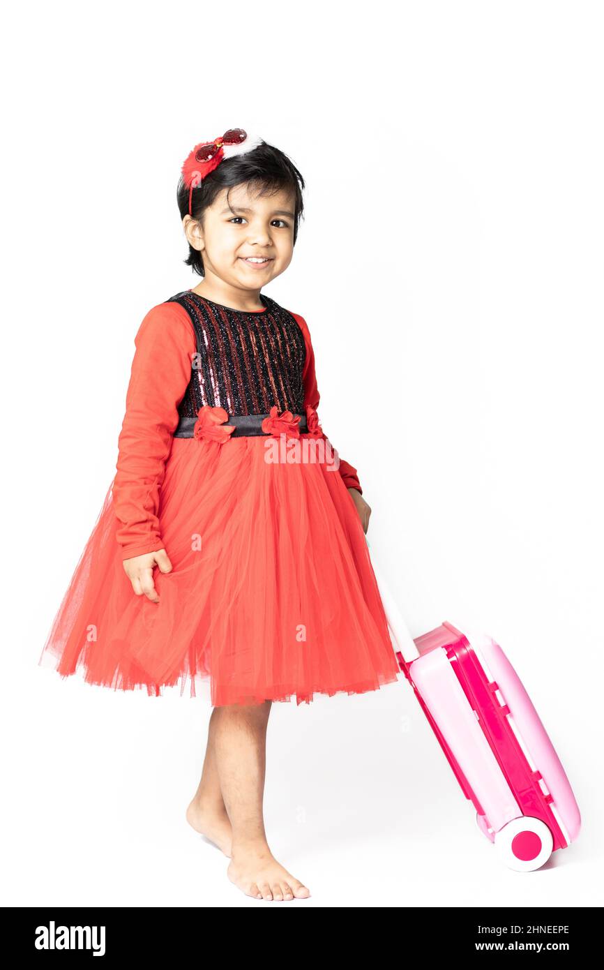 Asiatisch Indisch Hübsches Mädchen Kind In Rotem Kleid Posiert Mit Koffer-Gepäcktasche Auf Weißem Hintergrund. Spaß, Reisen, Tourist, Urlaub, Urlaub, Reise, Reise, Stockfoto