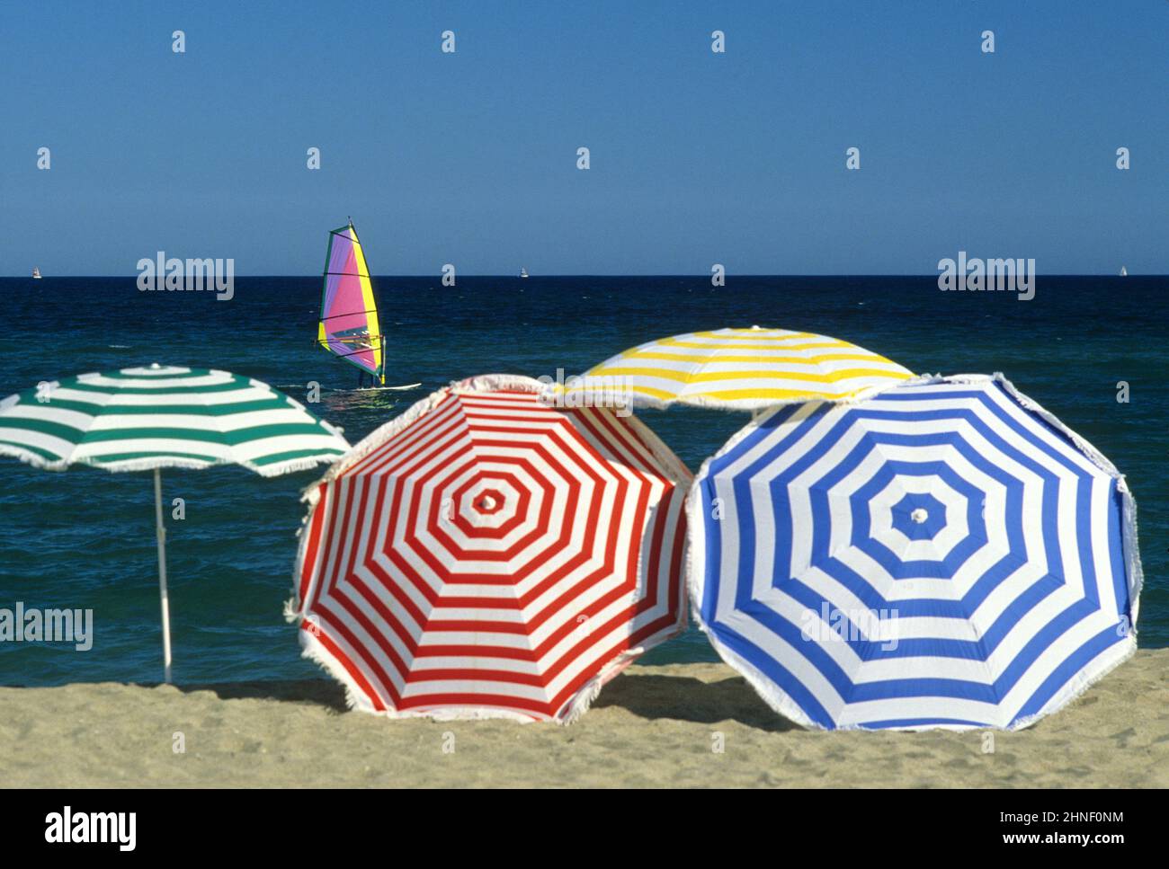 Mehrfarbige Regenschirme mit Strandgraphik, blauem Himmel und Meerwasser, Sommerurlaub Windsurfer Stockfoto