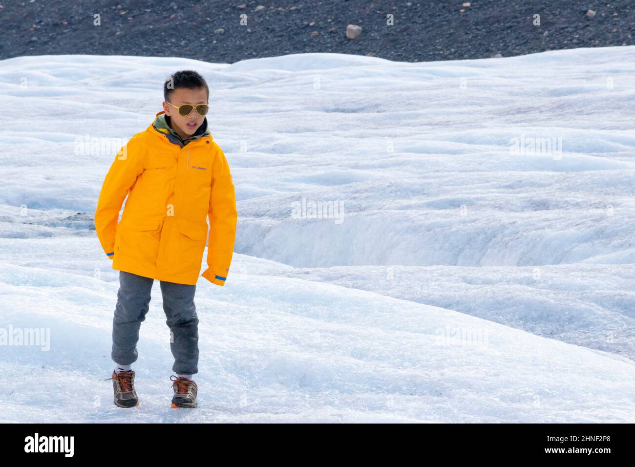 Asiatischer Junge in gelber Jacke und Sonnenbrille spielt gerne auf dem athabasca-Gletscher in der Nähe des Icefields parkway in der Nähe von Jaspis Alberta in kanada Stockfoto