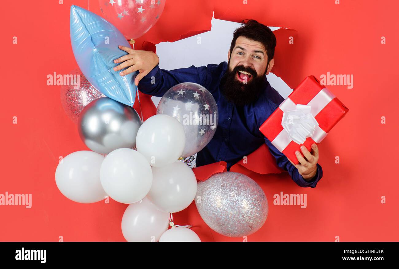 Geburtstagsfeier. Lächelnder bärtiger Mann mit Ballons hält ein Geschenk. Frohe Festtage, Jubiläum. Stockfoto