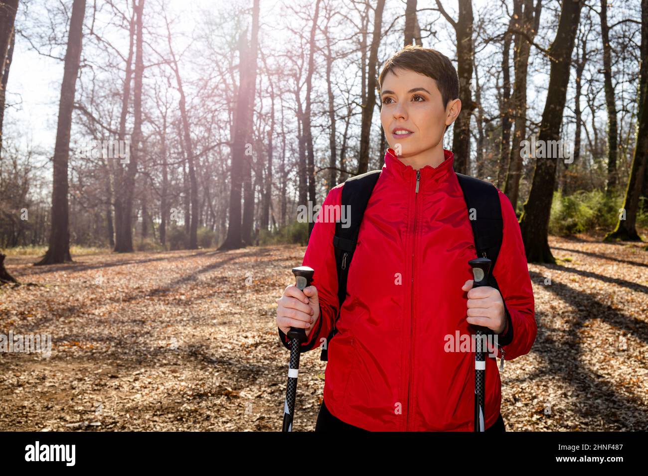 Die junge Frau macht eine Wanderung im Wald. Die Frau hat kurze Haare, trägt eine rote Jacke und verwendet Trekkingstöcke. Reise- und Outdoor-Life-Konzept. Stockfoto