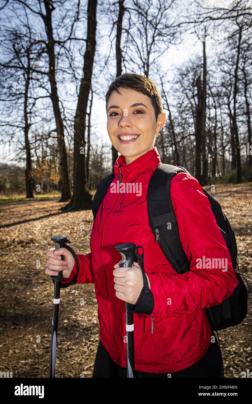 Die junge Frau macht eine Wanderung im Wald. Die Frau hat kurze Haare, trägt eine rote Jacke und verwendet Trekkingstöcke. Reise- und Outdoor-Life-Konzept Stockfoto