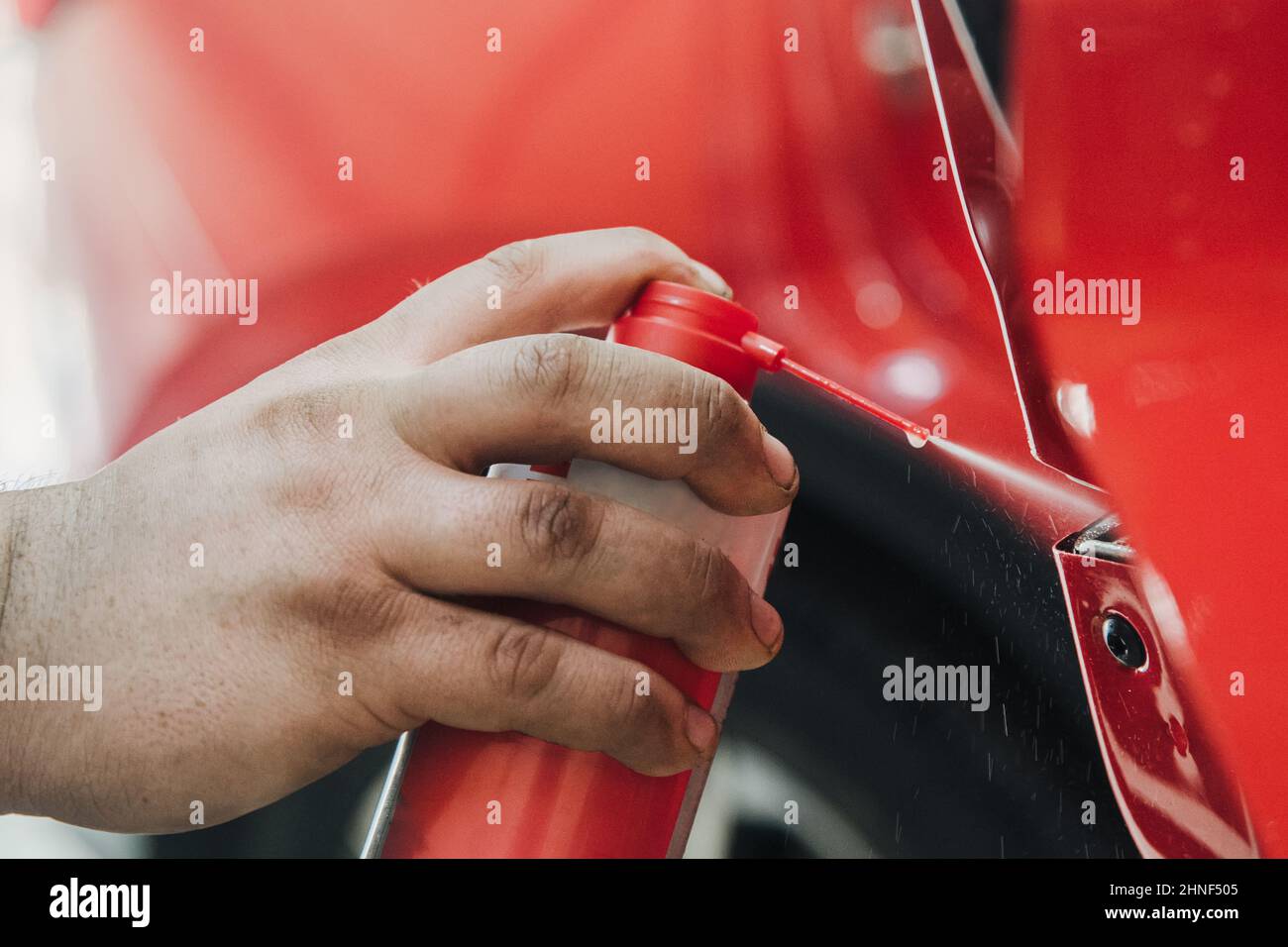 Sprühen von Fett aus einer Aerosoldose in geringer Schärfentiefe auf einen Türmechanismus des Autos Stockfoto
