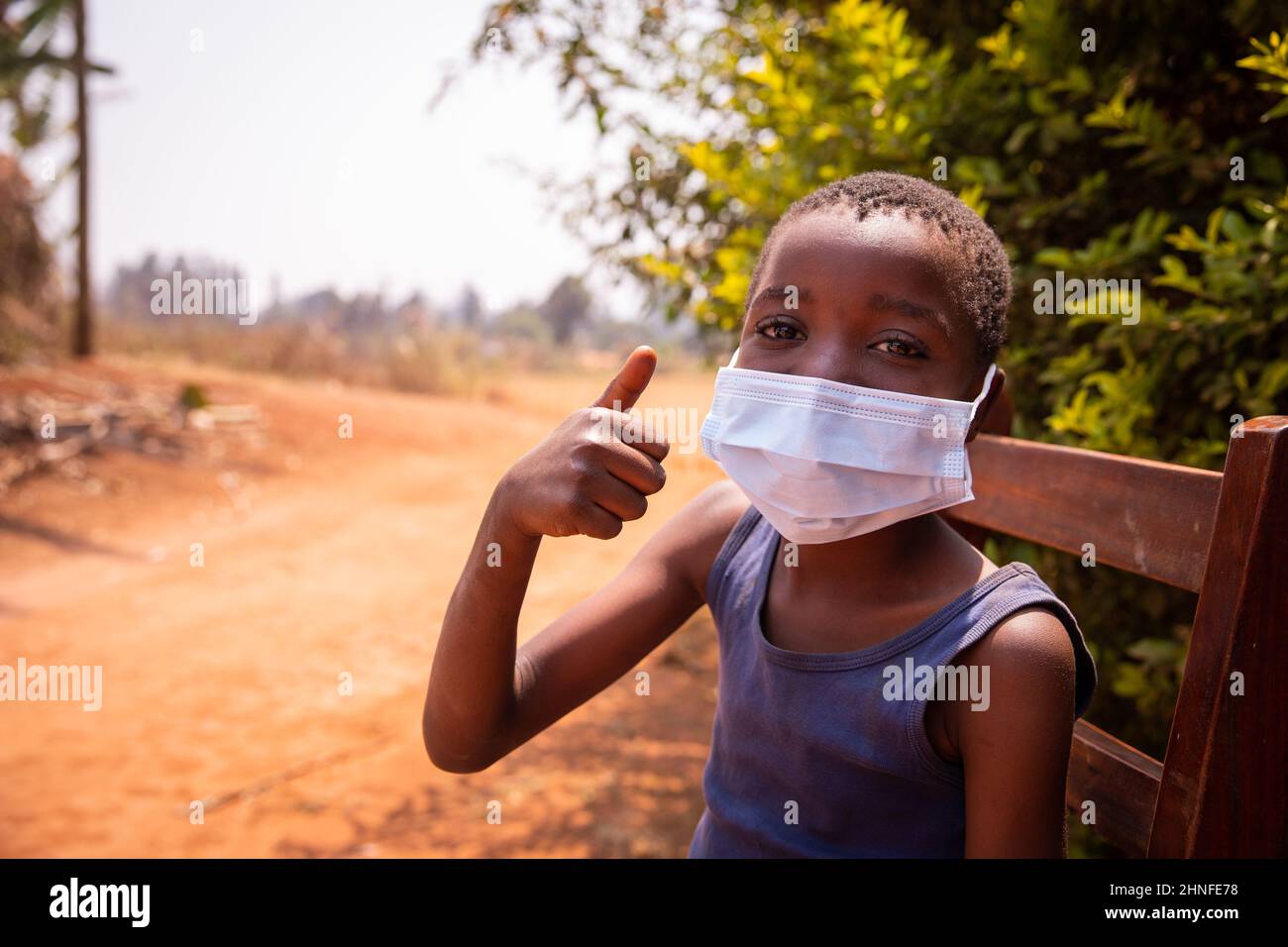 Glückliches afrikanisches Kind zeigt seinen Schwanz auf. Ein Kind trägt eine chirurgische Maske, um sich während der Coronavirus-Pandemie zu schützen - Konzept von covid-19 in Afrika Stockfoto