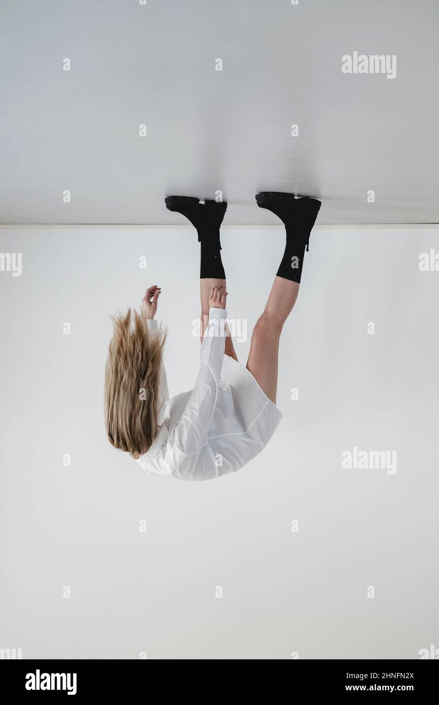Frau in schwarzen Stiefeln und weißem Hemd steht kopfüber im leeren Raum Stockfoto