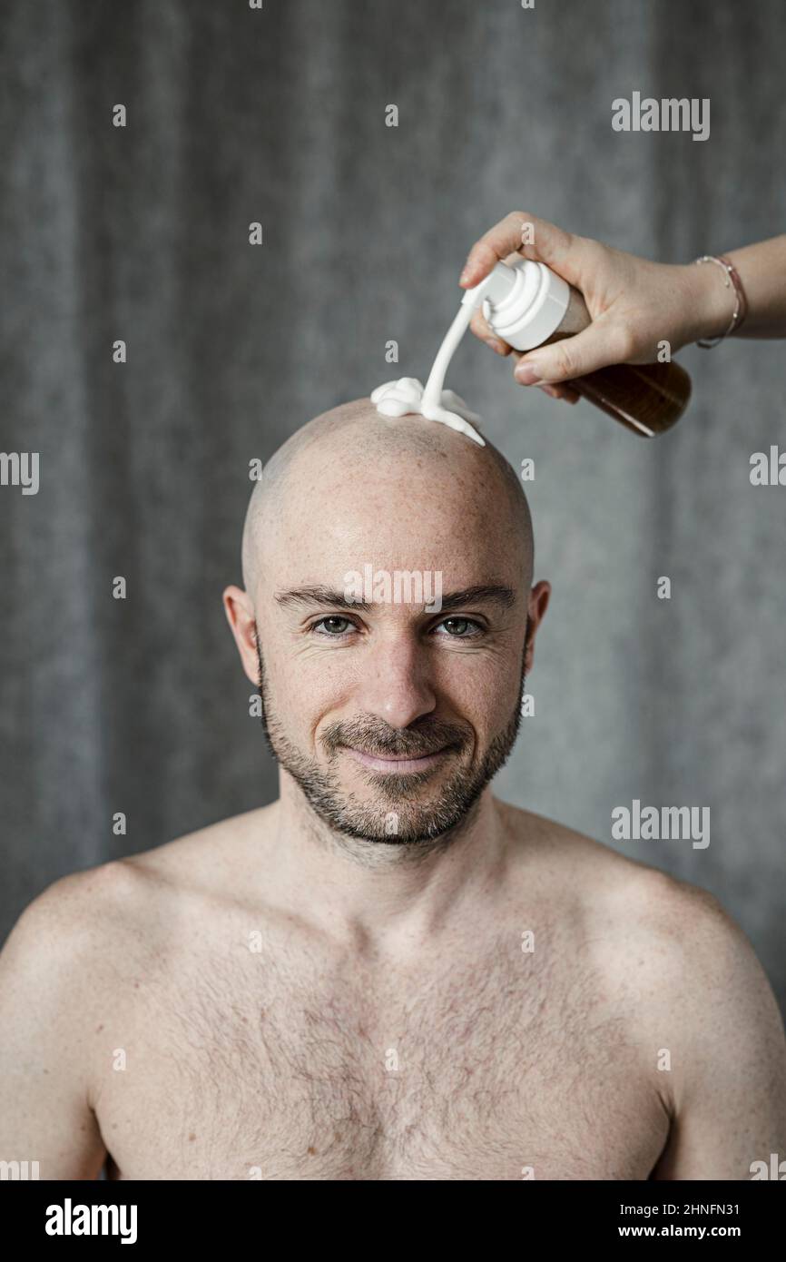 Der Mann bekommt Rasierschaum auf seinen kahlen Kopf gesprüht Stockfoto