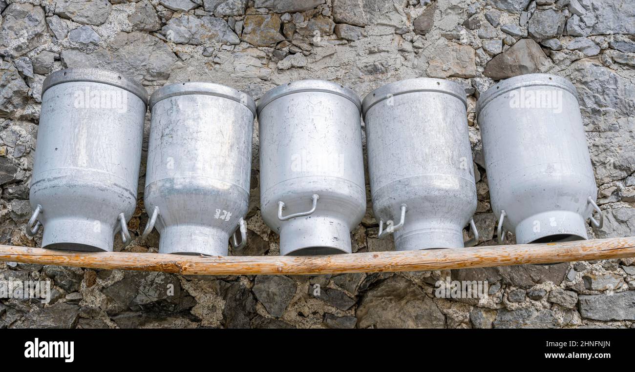 Milchdosen aufgereiht auf einer Holzbank, Fassade aus rauen Steinen einer Alm, Gramaialm, Alpenpark Karwendel, Tirol, Österreich Stockfoto
