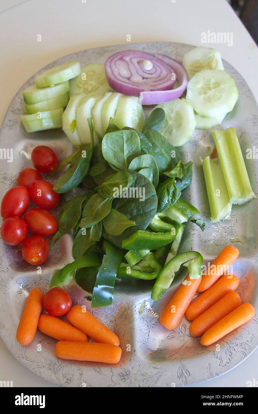 Eine silberne Platte mit buntem, rohem, biologischem Spinat, Gurken, Pflaumentomaten, Rote Zwiebeln, Babykarotten, Sellerie und grüne Paprika Stockfoto