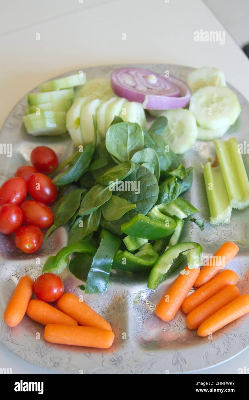 Eine silberne Platte mit rohem, biologischem Spinat, Gurken, Pflaumentomaten, roten Zwiebeln, Baby Karotten, Sellerie und grüne Paprika, ein Vegeta Stockfoto