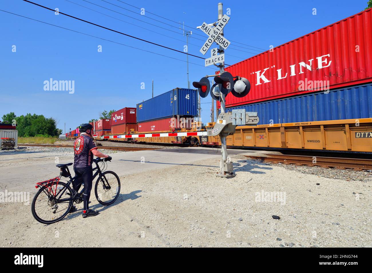 Bartlett, Illinois, USA. Ein einsamer Radfahrer wartet an einer Bahnüberfahrt auf einen intermodalen Güterzug der Canadian National Railway. Stockfoto