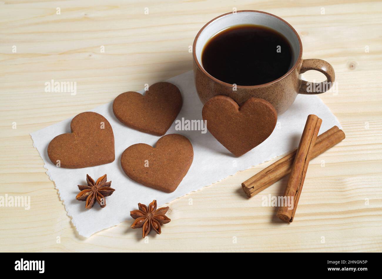 Tasse Kaffee, herzförmige Ingwerkekse, Zimt und Anisstern auf einem Holztisch Stockfoto
