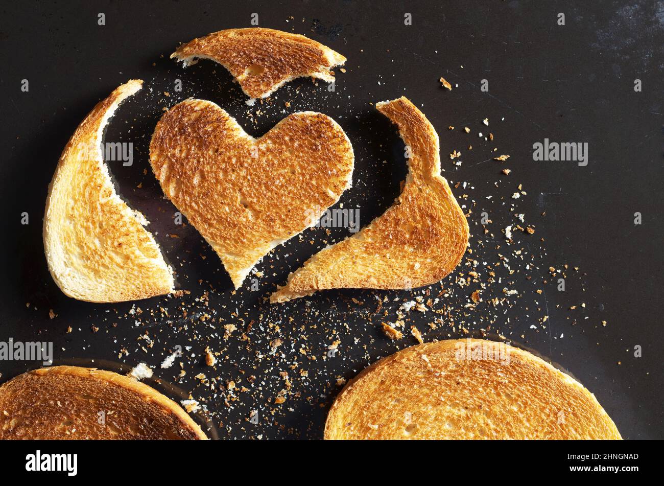Stück gebratenes Brot in Herzform und Scheiben mit Krümel auf schwarzem, altem Metallic-Hintergrund, Draufsicht Stockfoto