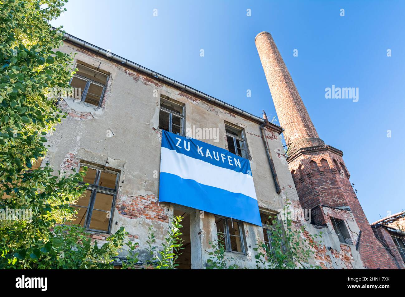 Fassade eines malerischen alten Fabrikgebäudes mit Kamin und zum Verkauf Schild Stockfoto