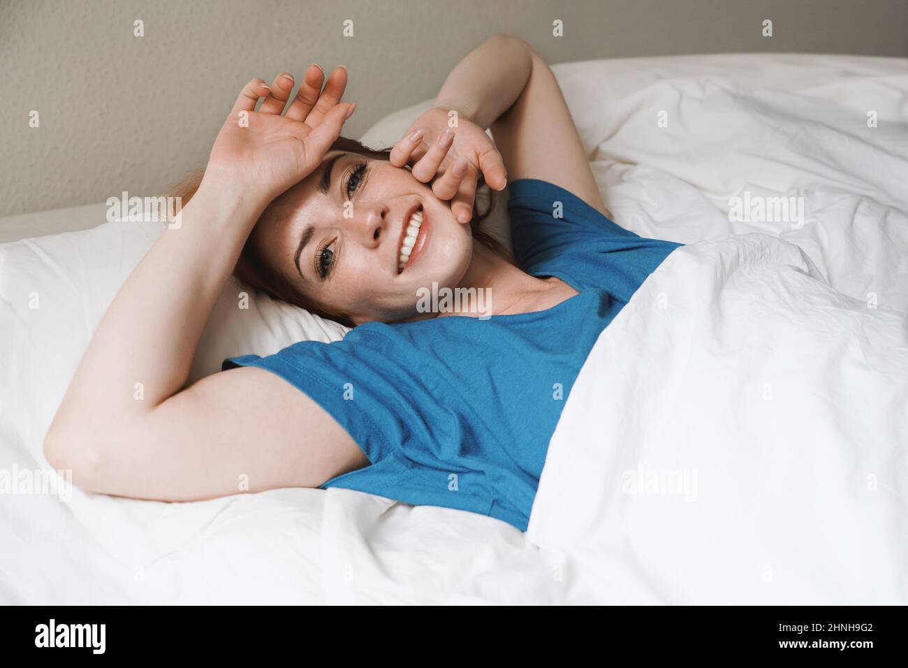 Steh auf und glänze - ausgerustete junge Frau im Bett wacht lächelnd auf Stockfoto