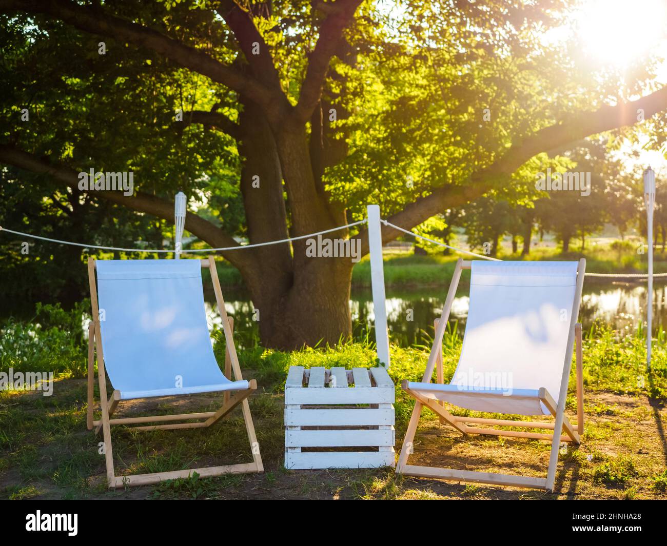 Zwei weiße Strandsessel und Holzkiste als Tisch dazwischen auf der Natur am Seeufer, Städtereise und Platz zum Entspannen Stockfoto