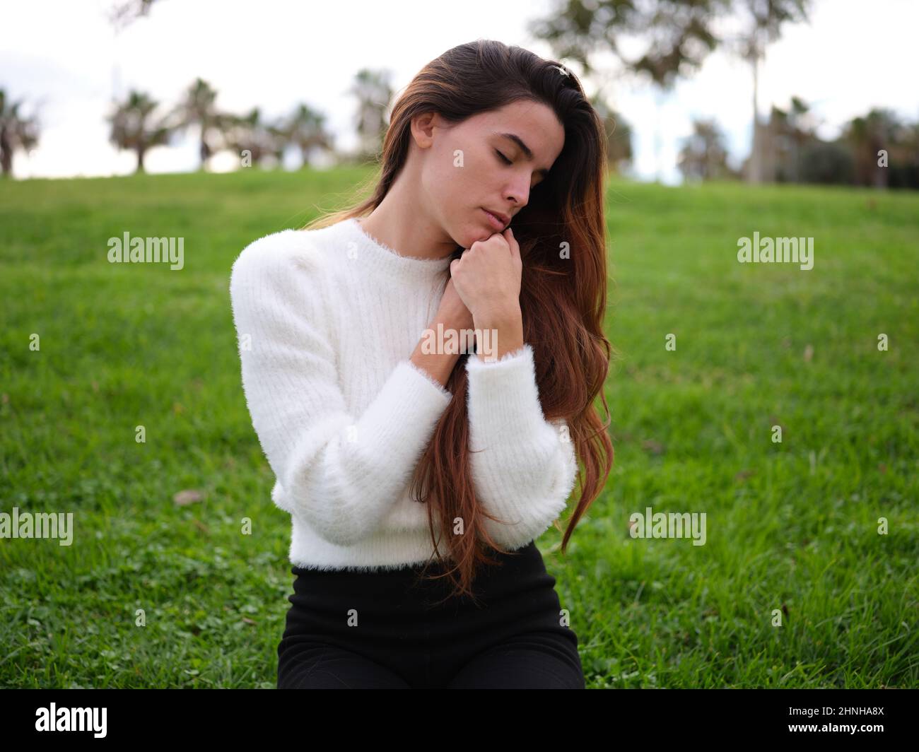 Eine junge Frau, die sich im Park entspannt, ihre Hände auf der Brust gefaltet und ihre Augen geschlossen. Stockfoto