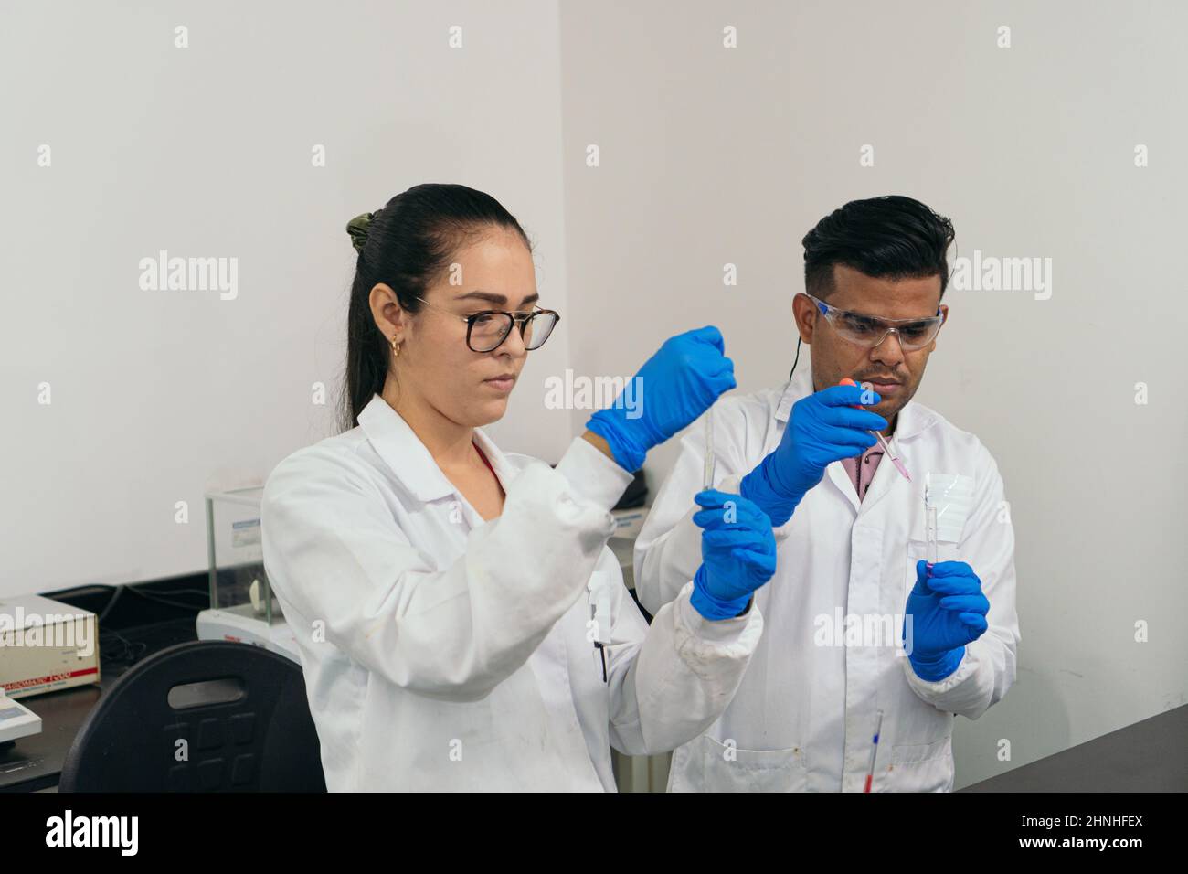 Labortechniker, die chemische Tests durchführen. Wissenschaftler tragen Schutzhandschuhe, Schutzbrille und weiße Mäntel. Labor- und Chemiekonzept Stockfoto