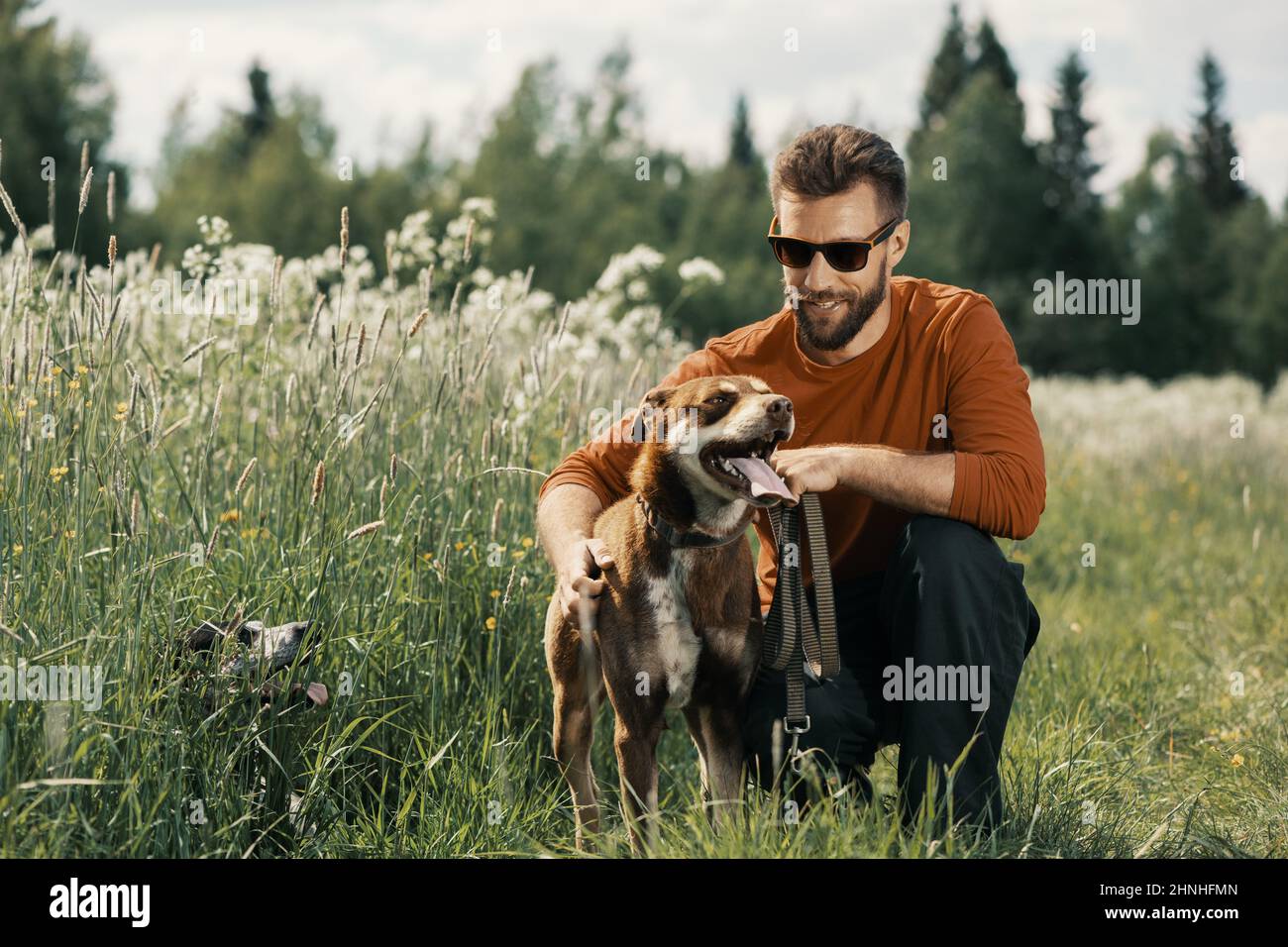 Lächelnder kaukasischer Mann umarmt glücklichen Hund im Freien. Stockfoto