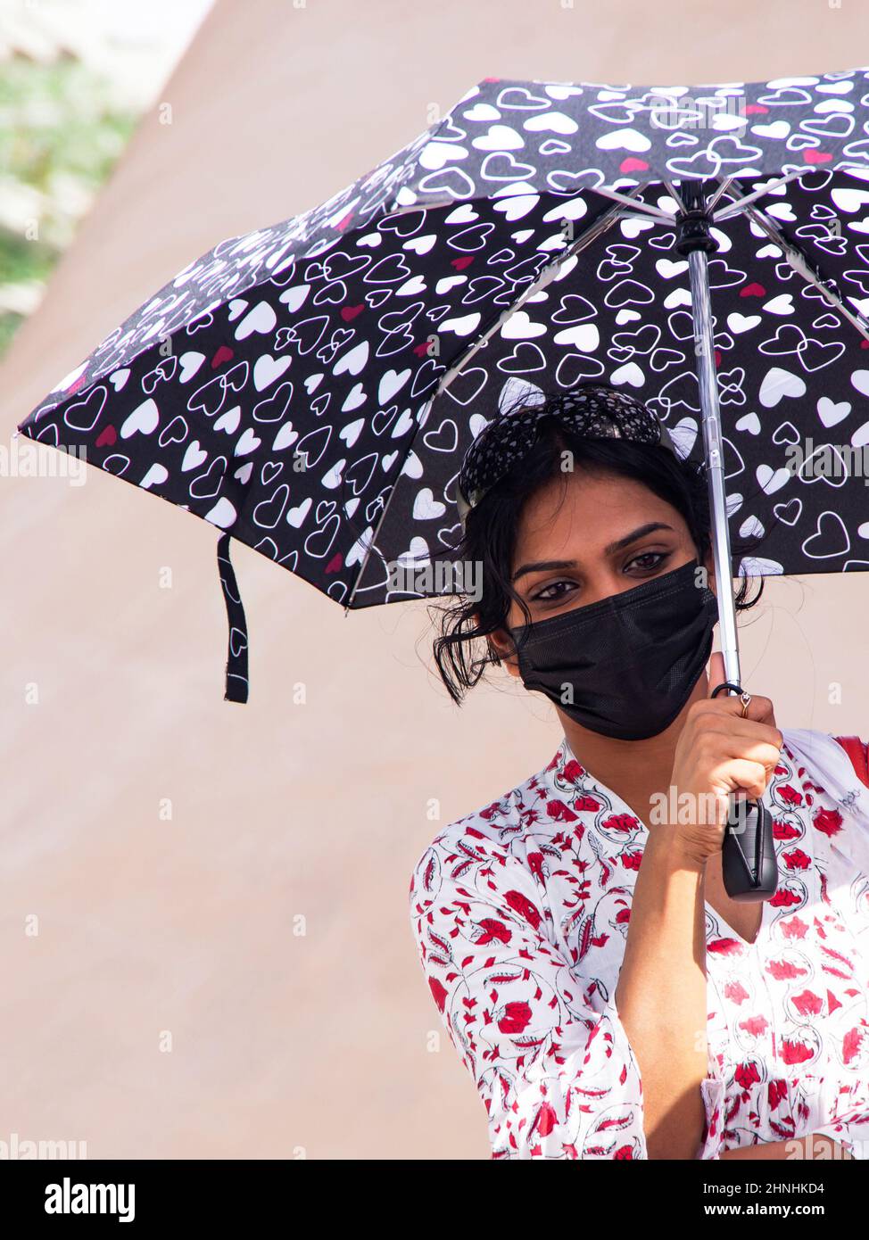 Tausendjährige Frau mit einem gemusterten Regenschirm in einer medizinischen Maske Stockfoto