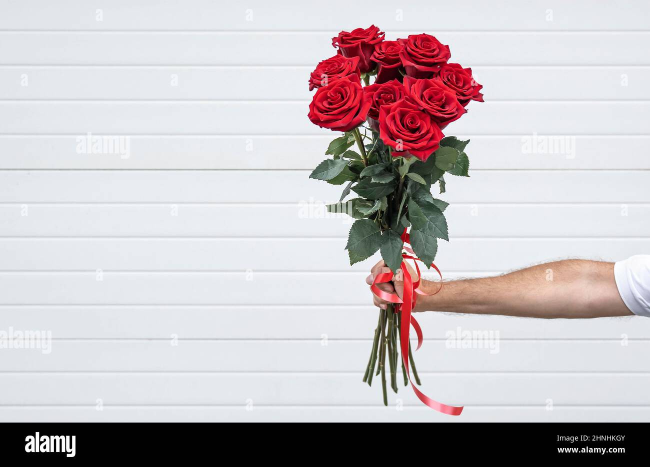 Blumenstrauß in der Hand auf hellem Hintergrund. Gentleman mit einem Strauß roter Rosen. Stockfoto