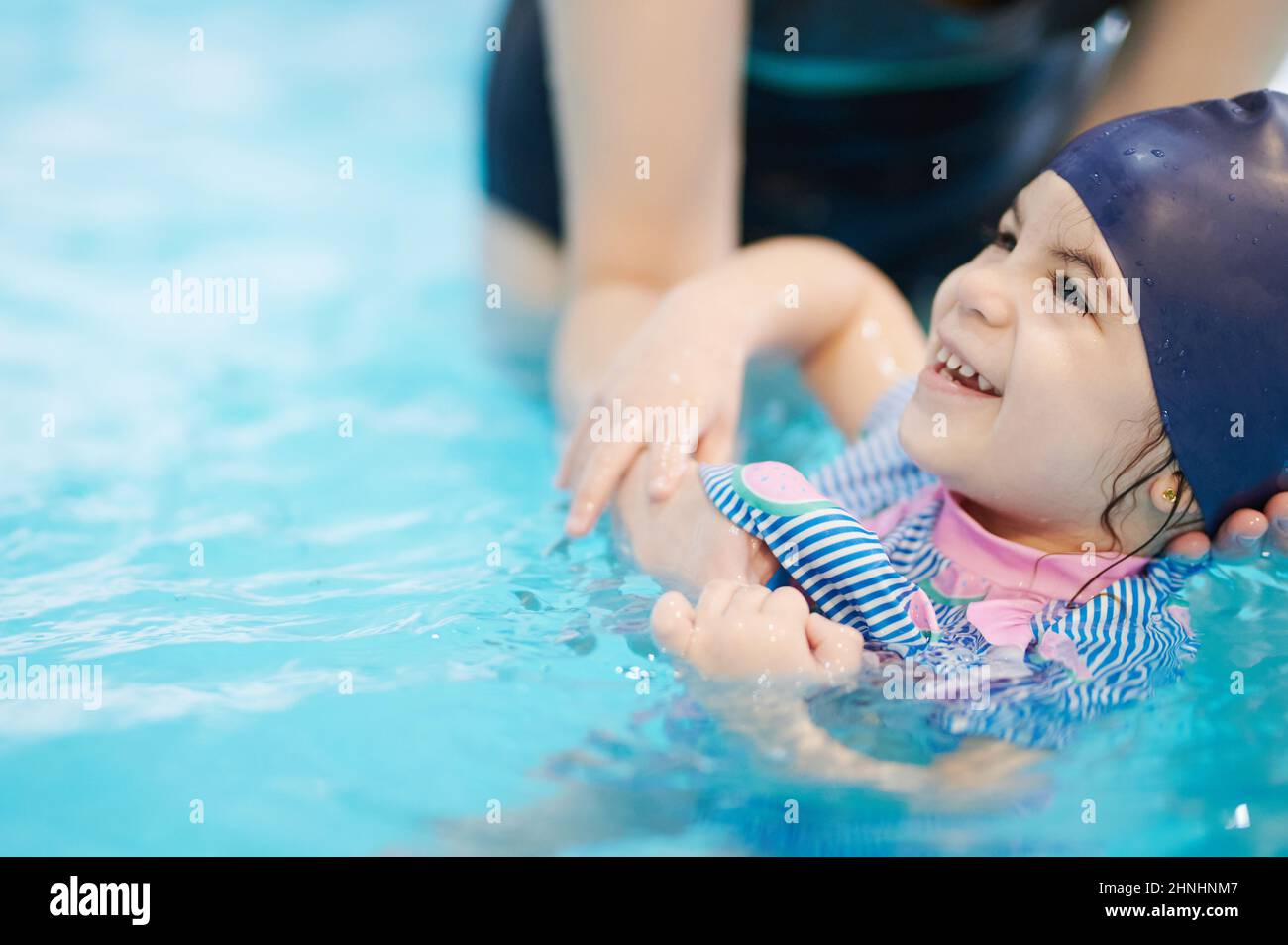 Glückliches Kind, das mit Unterstützung des Lehrers in der Schule schwimmen lernt Stockfoto