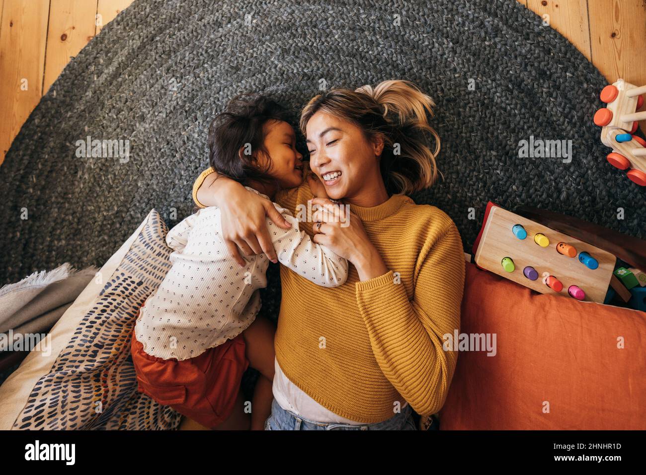 Ansicht von oben einer Mutter und ihrer Tochter, die auf dem Boden in ihrem Spielbereich liegen. Liebevolle Mutter lächelt fröhlich, während sie ihre Tochter umarmt. Mo Stockfoto