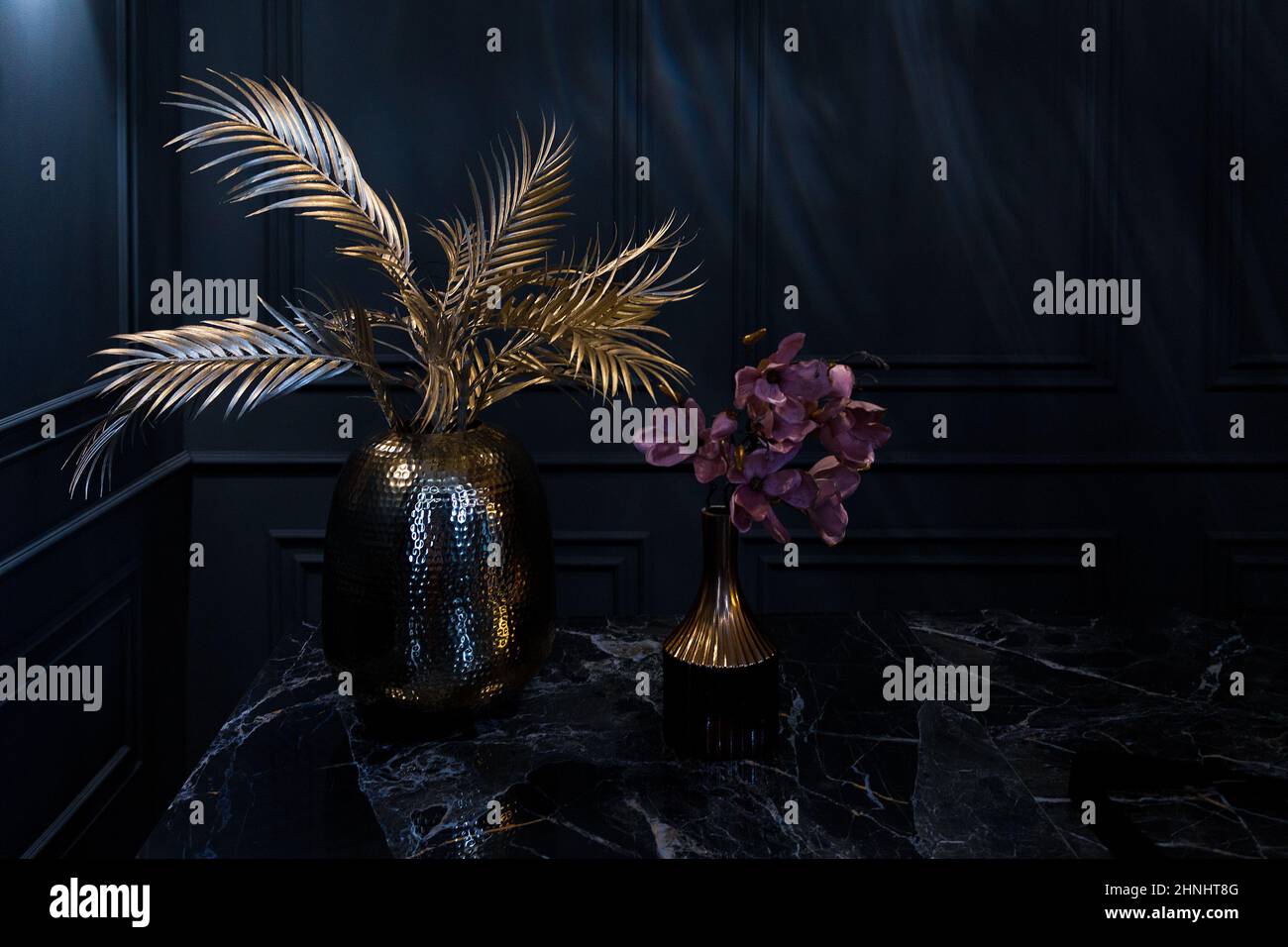 Dunkles Zimmer mit dekorativer Vase, die auf einem mit Blumen geschmückten Tisch platziert ist Stockfoto