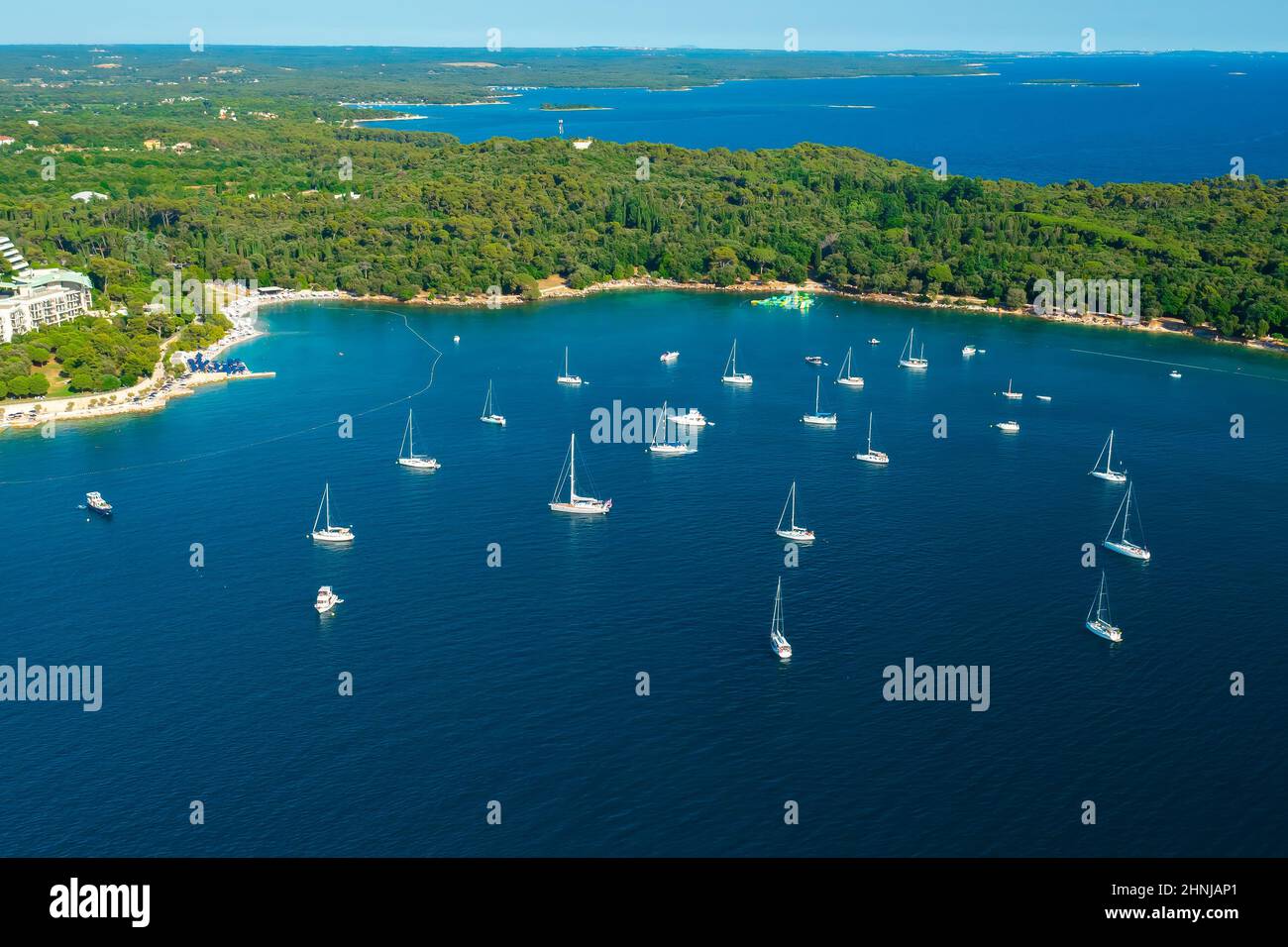 Luxuriöse Yachten treiben auf der ruhigen Oberfläche der Adriatischen Meeresbucht in der Nähe der Halbinsel. Dichte grüne Wälder umgeben die kroatische Stadt Rovinj. Luftpanorama Stockfoto