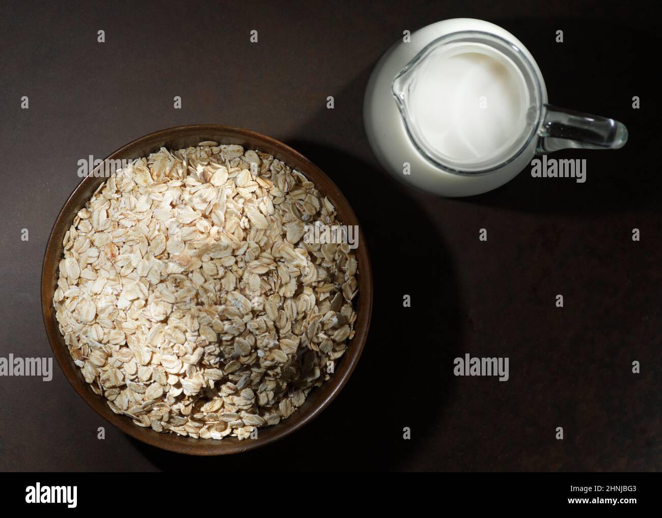 Haferflocken in einer Holzschüssel, Haferflocken und eine Tasse Milch auf dem Tisch. Gesunde Ernährung Stockfoto