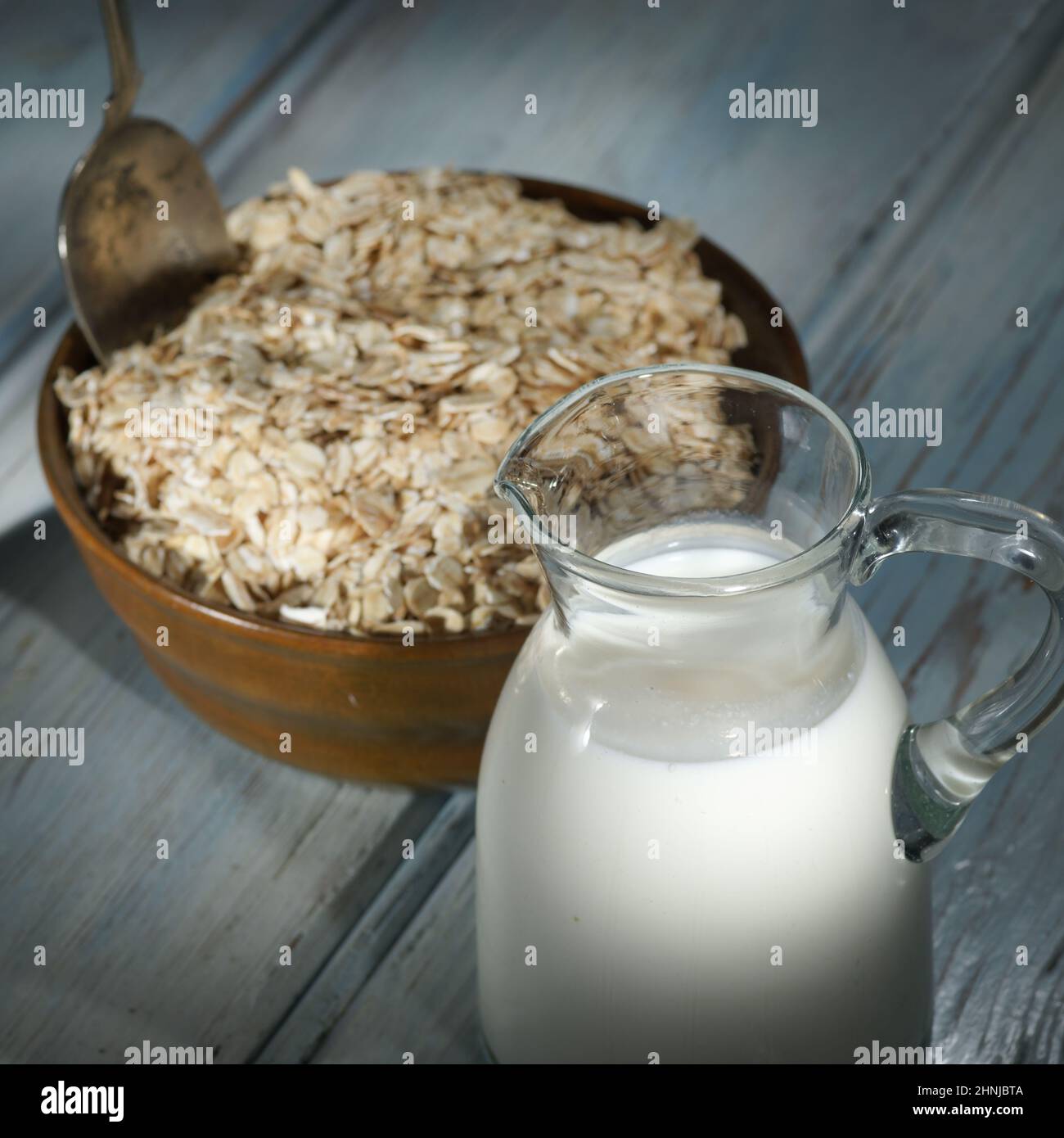 Haferflocken in einer Holzschüssel, Haferflocken und eine Tasse Milch auf dem Tisch. Gesunde Ernährung Stockfoto