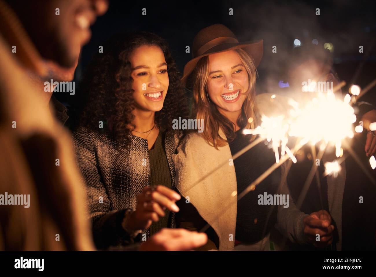 Multikulturelle, beste Freunde auf einer Dachparty, die lächelt und Funkler beleuchtet. Nachts, stilvolle Party Stockfoto