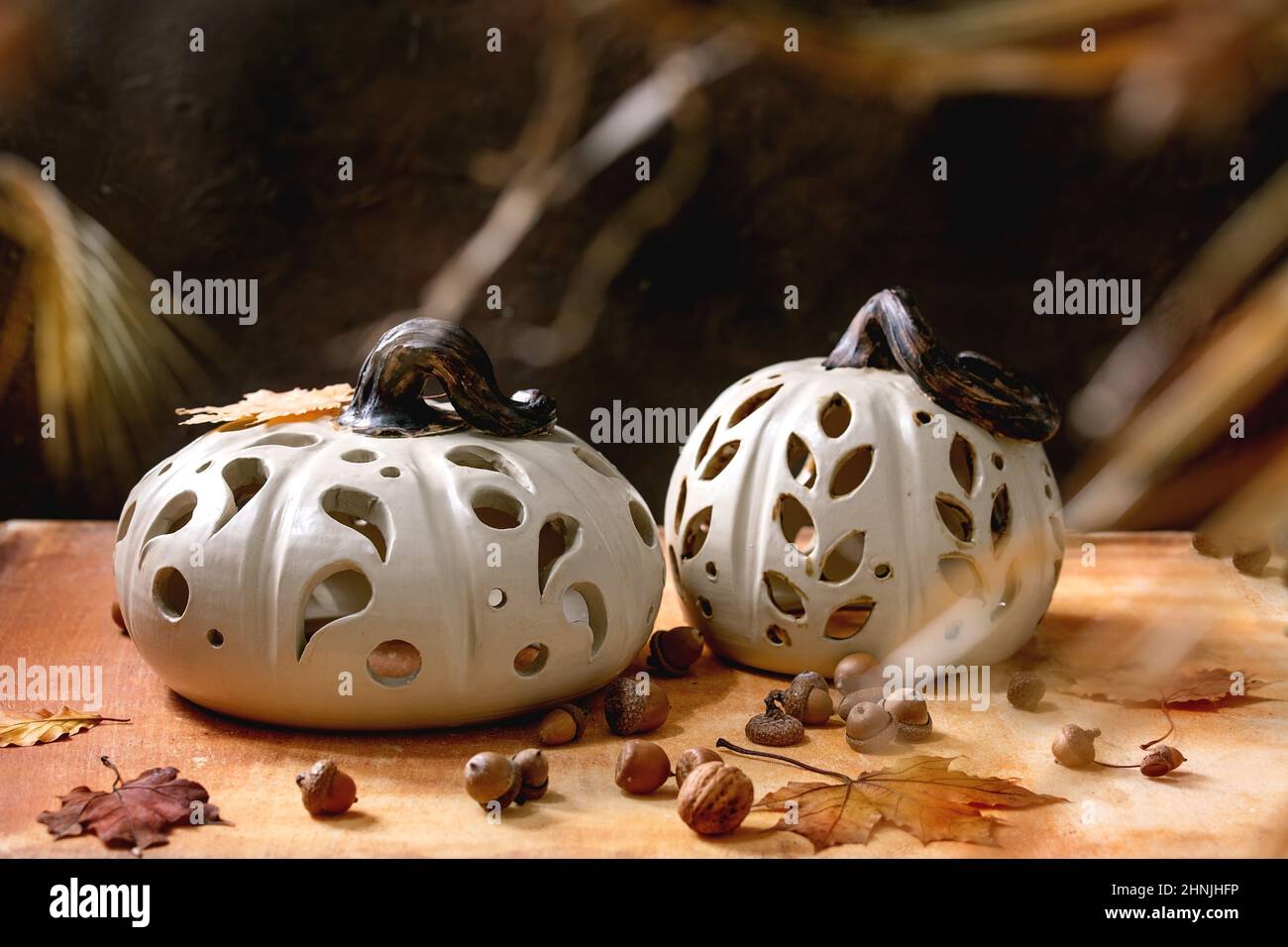 Halloween- oder Thanksgiving-Dekorationen, Set aus weißen handgefertigten geschnitzten Keramik-Kürbissen, die auf einem orangefarbenen Steintisch mit Herbstblättern und Eicheln stehen. Stockfoto