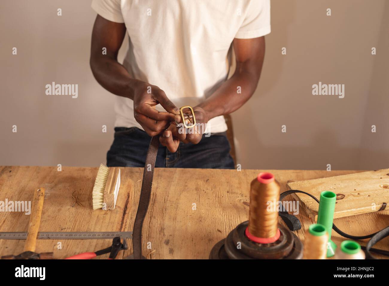 Mittelteil des afroamerikanischen jungen männlichen Handwerkers, der Schnalle auf Ledergürtel in der Werkstatt fixiert Stockfoto