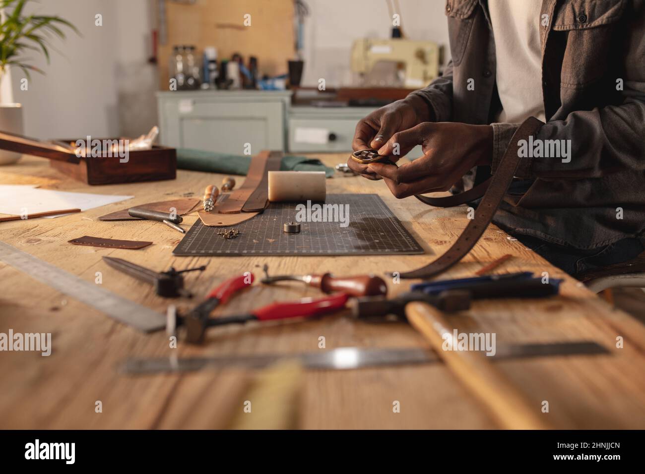 Mittelteil des afroamerikanischen jungen Handwerkers, der Schnalle am Ledergürtel in der Lederwerkstatt fixiert Stockfoto