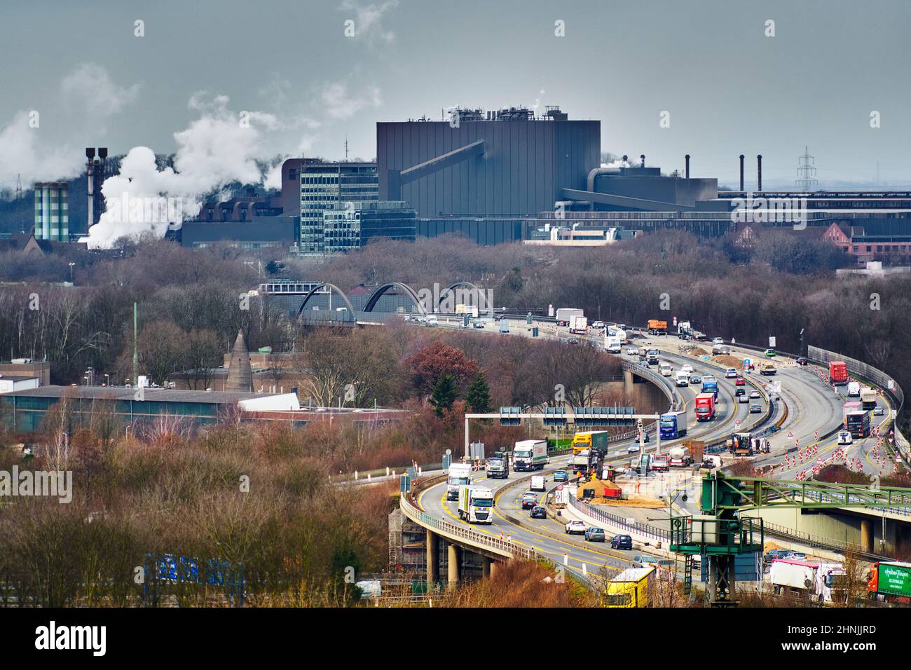 Duisburg, 9. Februar 2022: Autobahn mit regem Verkehr durch das Ruhrgebiet vor einem großen Industriewerk Stockfoto
