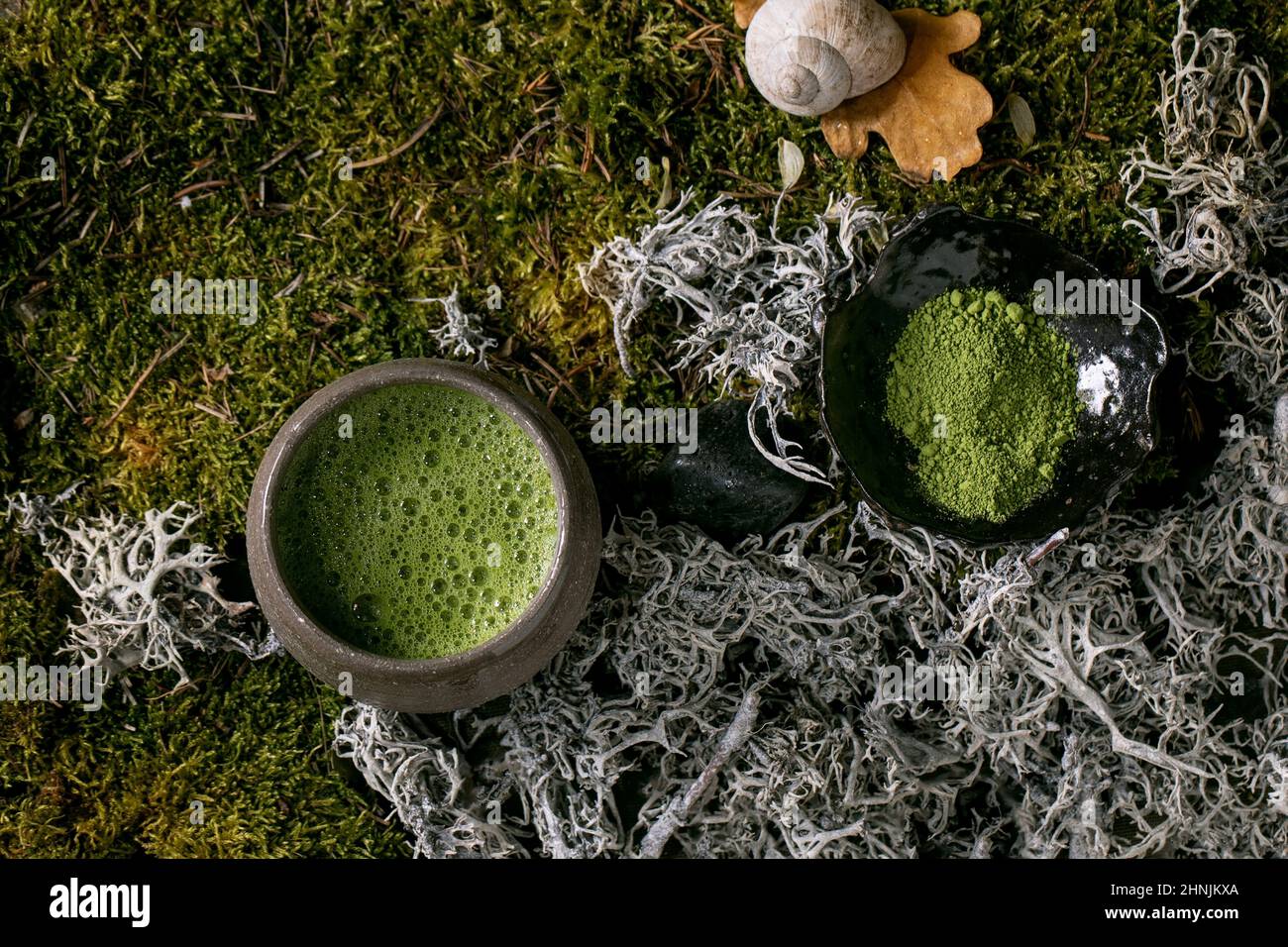 Traditionelle japanische heiße grüne schaumige Tee-Matcha in Keramikbecher und pulverförmige Matcha über Waldmoos als Hintergrund. Gesundes natürliches Getränk. Draufsicht Stockfoto