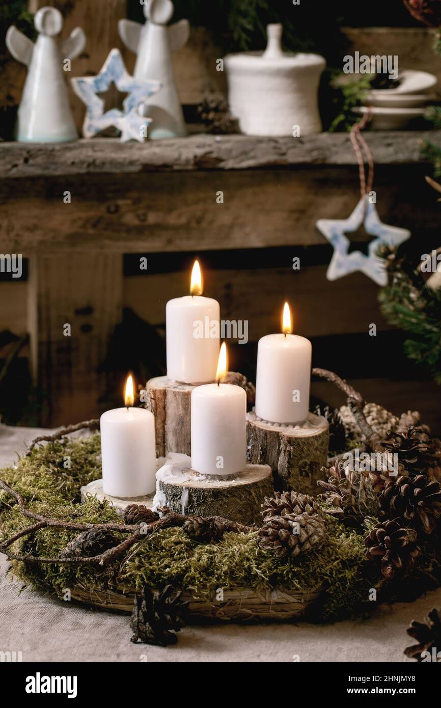 Weihnachtliche Einrichtung im rustikalen Stil. DIY Naturmoos Kranz und Advent brennende Kerzen auf dem Tisch. Handwerk Keramik und Geschenk-Boxen auf Holz pa Stockfoto