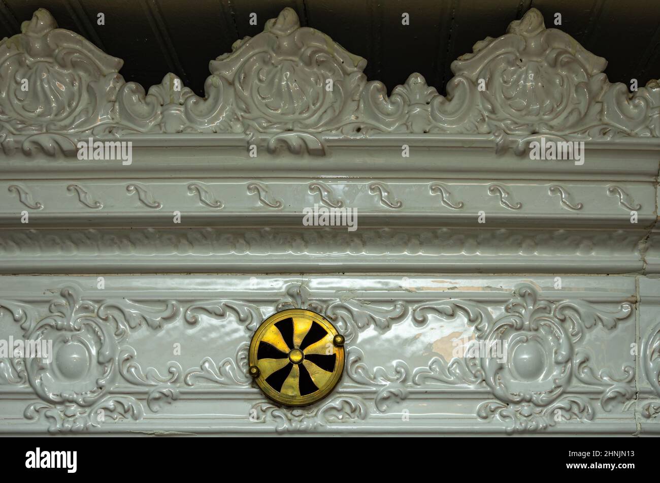 Detail des oberen Randes eines Kachelofens im Barock-klassizistischen Design mit Lüftungsregler. Stockfoto
