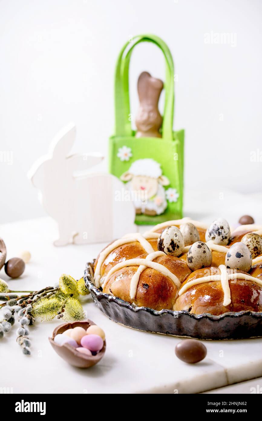 Hausgemachte Ostern traditionelle heiße Kreuz Brötchen in Keramikschale mit Blüten, Schokolade banny, Süßigkeiten und Wachteleiern auf weißem Marmortisch. Ostern h Stockfoto