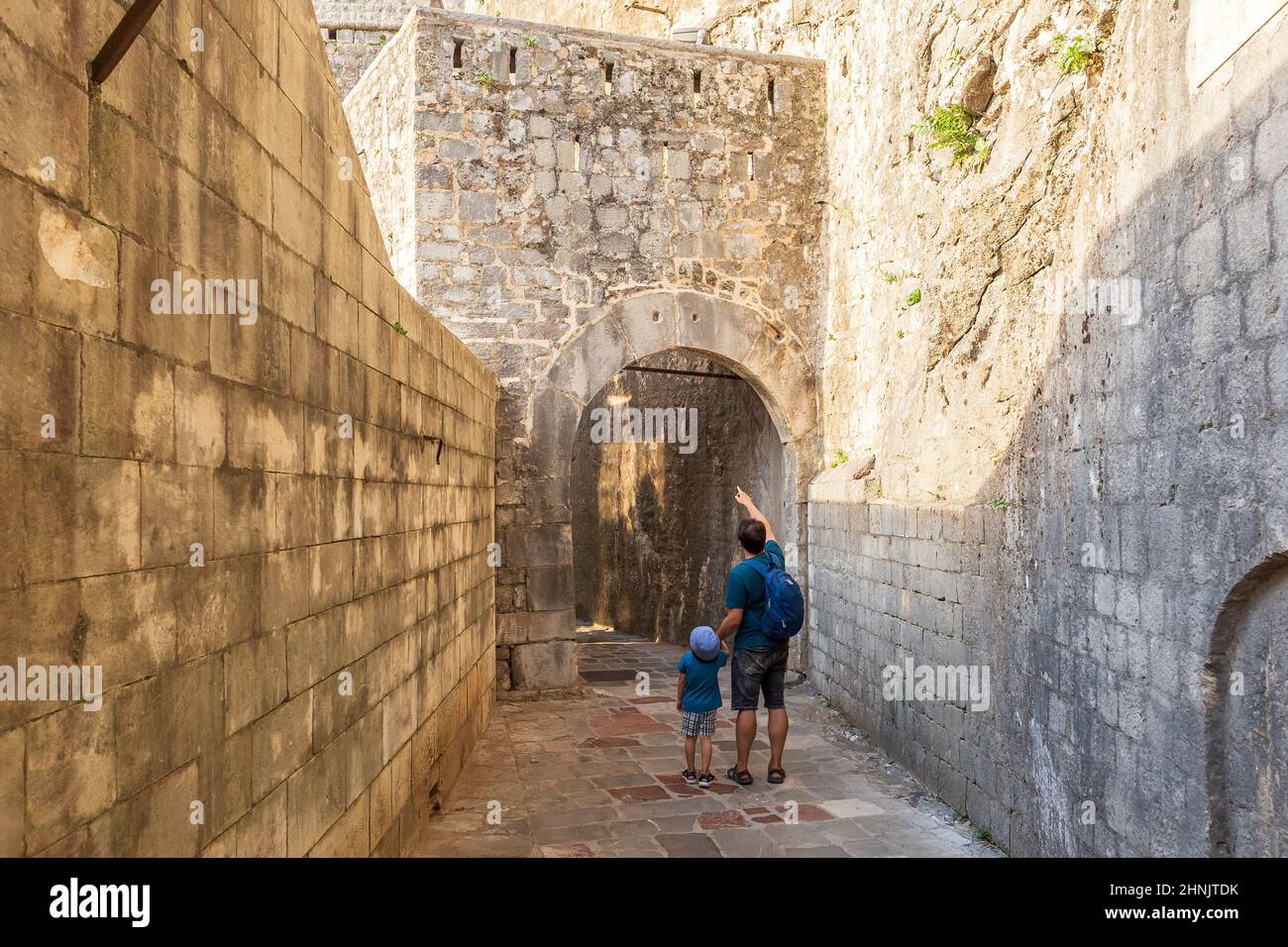 Vater und Sohn gehen durch mittelalterliche Festungsmauern in Kotor, Montenegro. Touristen, die auf einem Summ die enge gepflasterter Steinstraße in der Altstadt erkunden Stockfoto